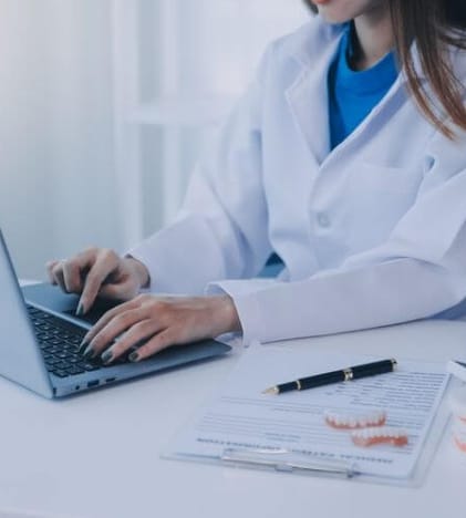 Dentist typing on her laptop at her desk with papers and model teeth
